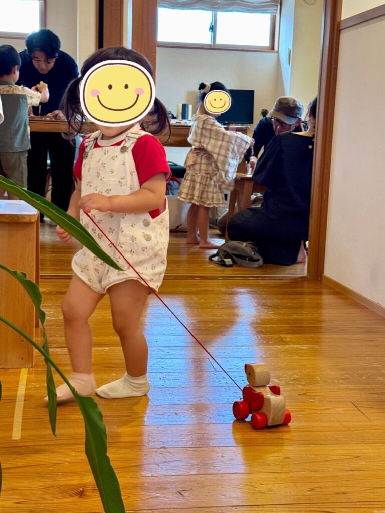 ひだまりフェスの会場で、無垢床の上を木のおもちゃを引いて歩く小さな子ども