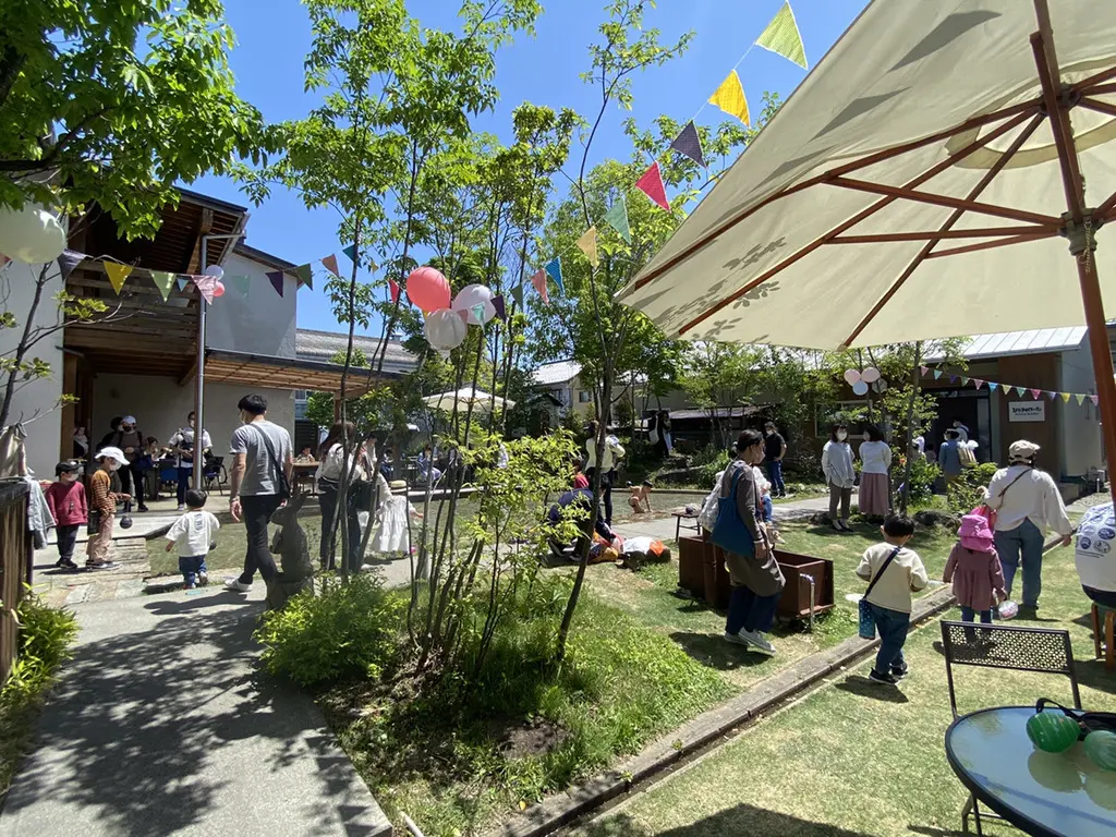晴天の下で開催されたひだまりフェスの屋外会場。庭にガーランドや風船が飾られ、来場者の家族連れが集まっている様子
