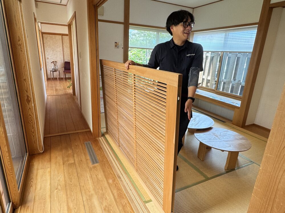 スタッフが取り外した木製の格子パネルを抱えて、メンテナンス方法を実演している様子