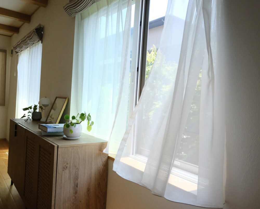 春から夏に窓を開けて風を通す、レースカーテンが揺れる無垢床のリビング
